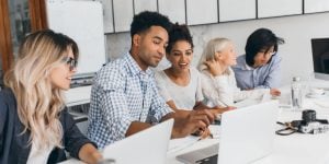 Students sitting in front of laptops, talking to one another and pointing at their laptop screens